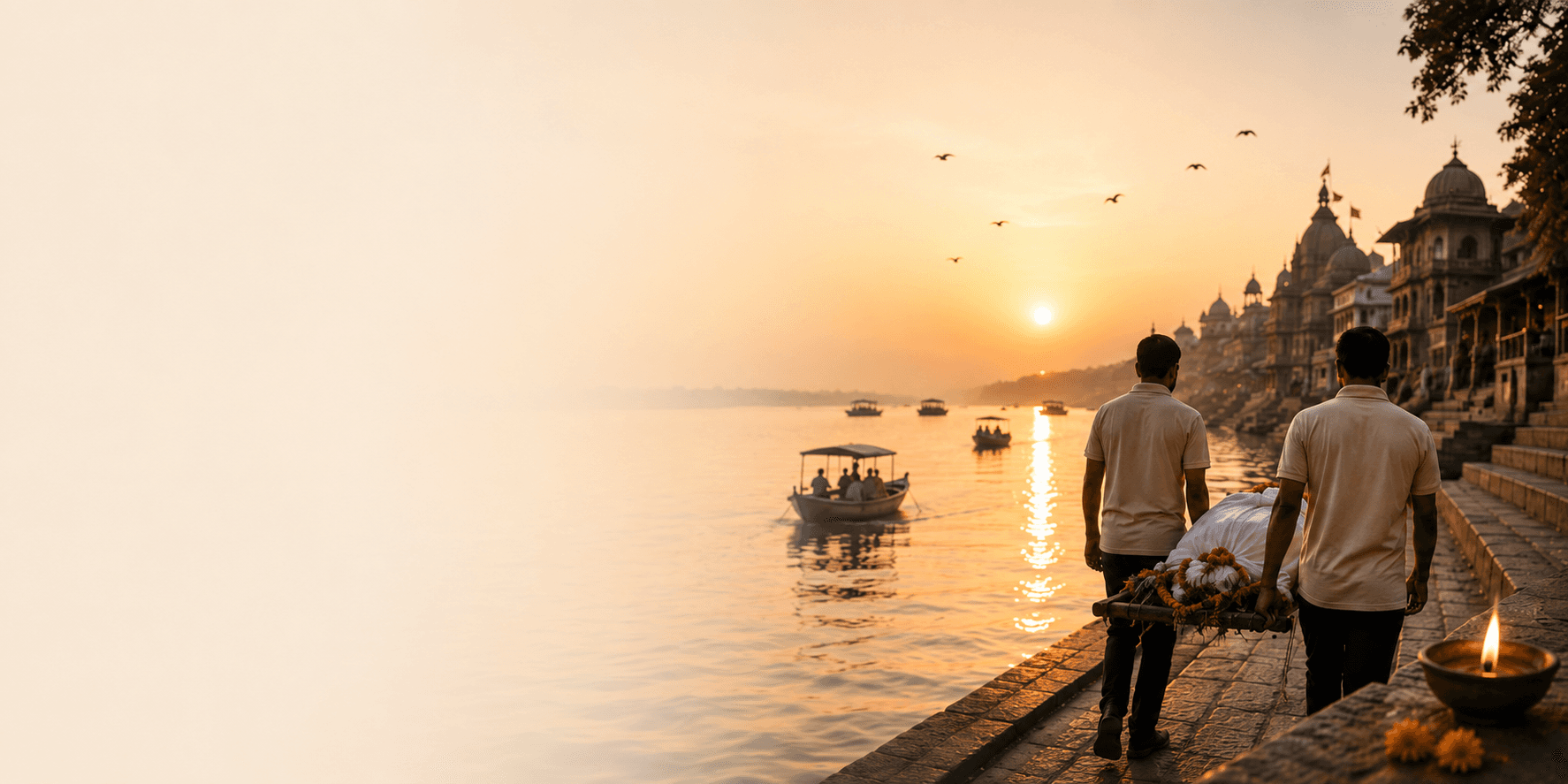Two Moksha Sewa volunteers carrying a body along a river ghat at sunset